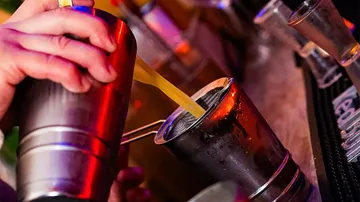 Bartender pouring drink through strainer at bar.