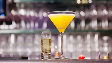 Gelber Cocktail und Schnapsglas auf Bartheke.