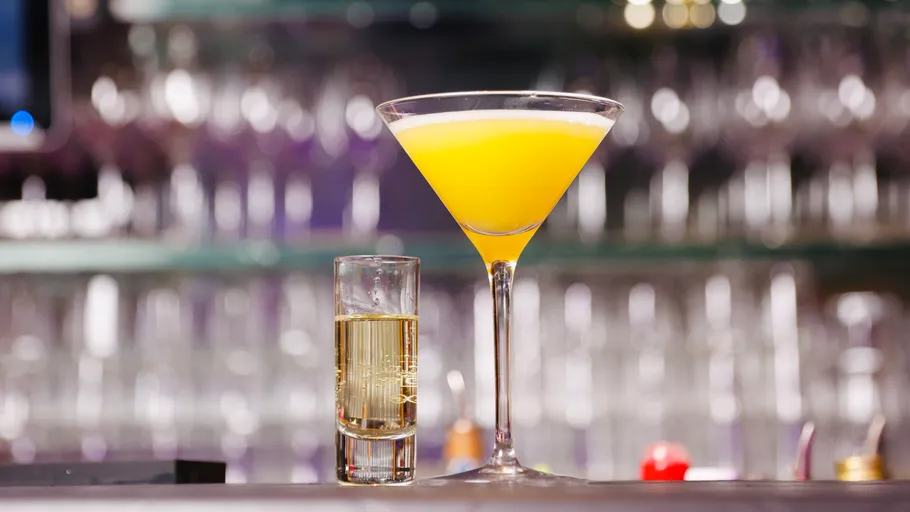 Gelber Cocktail und Schnapsglas auf Bartheke.