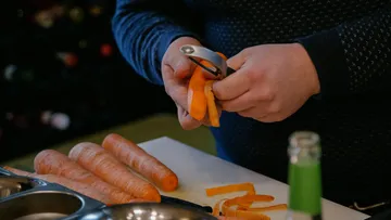 Person schält Karotten auf Küchentheke.