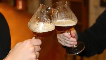 Two hands clinking beer glasses indoors.