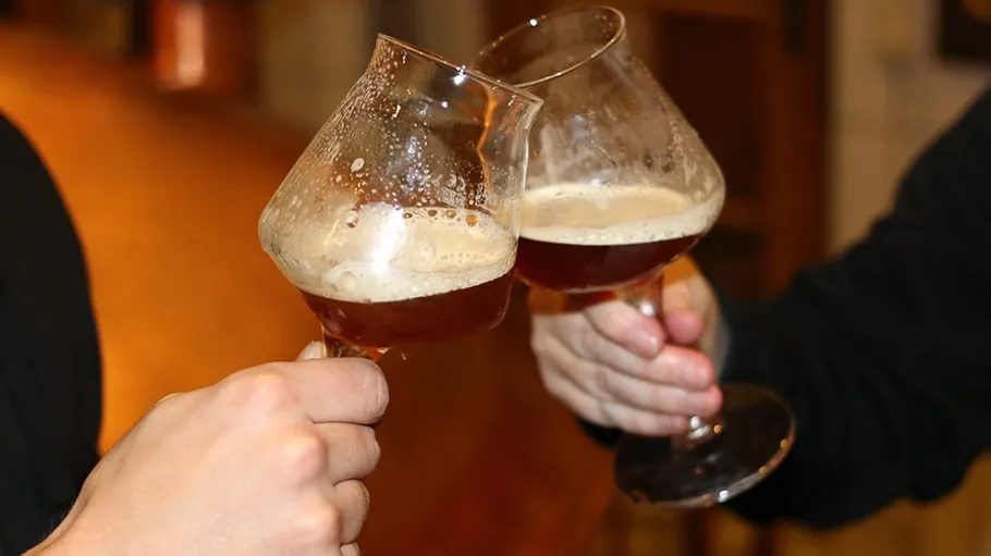 Two hands clinking beer glasses indoors.