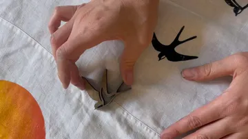 Hände ordnen vogelartige Dekoration auf Stoff an.