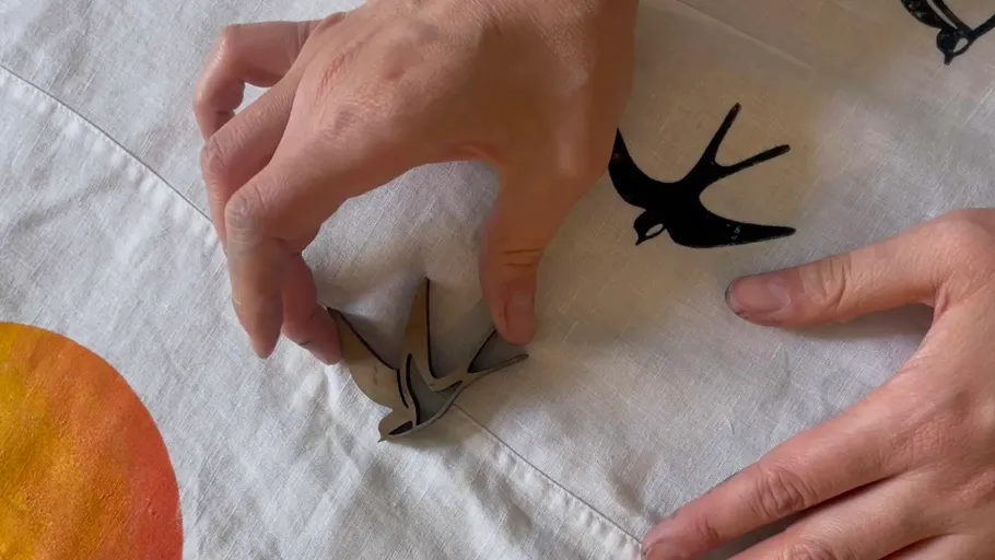 Hands arranging bird-shaped decoration on fabric.