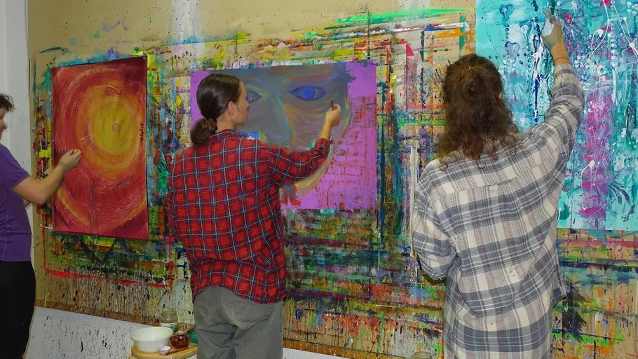 Three people painting on a colorful wall.
