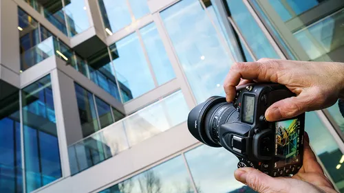 Camera held photographing modern glass building.