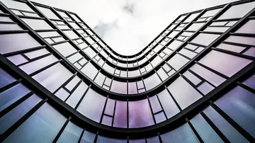 Curved glass building with cloudy sky.