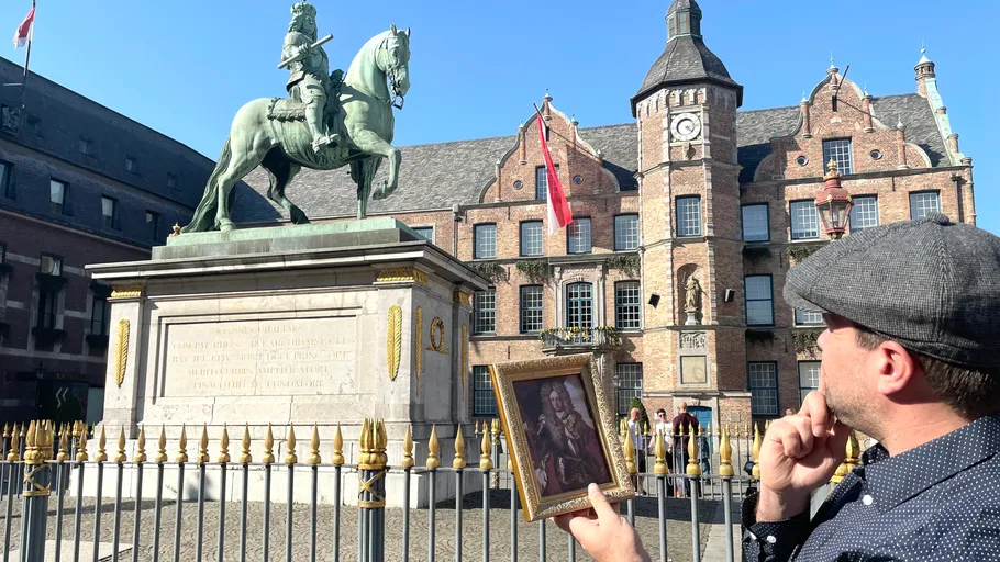 Mann hält Porträt vor Reiterstatue, historisches Gebäude.