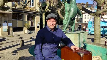Man sitting near statue with suitcase outdoors.