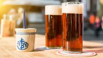 Two beer glasses on a wooden table outdoors.