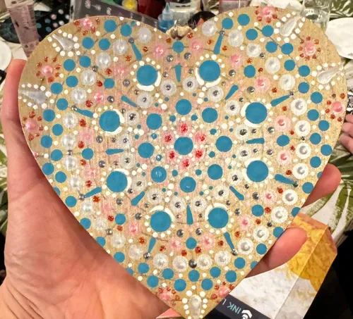 Hand holds decorated wooden heart shape.