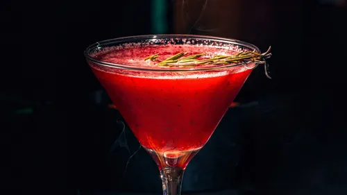 Red cocktail garnished with rosemary sprig.