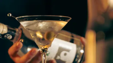 Martini with olive in glass, bottle nearby.