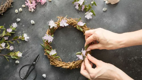 Hands crafting floral wreath on dark surface.