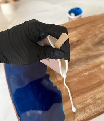 Hand pours resin on wooden board.