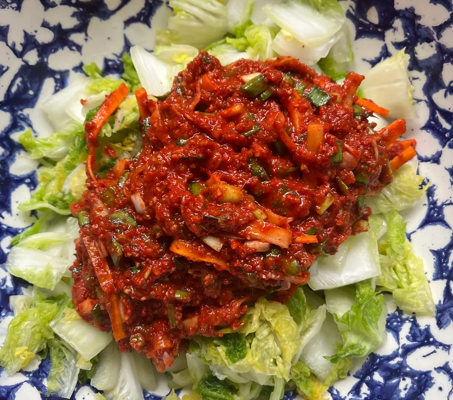 Spicy red sauce on chopped cabbage in bowl.
