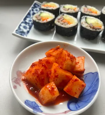 Kimchi in a bowl, sushi rolls behind.