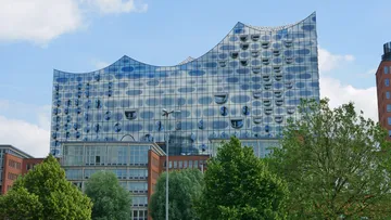 Modernes Glasgebäude mit geschwungenem Dach und Bäumen.