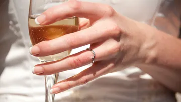 Hand hält Sektglas, trägt Ring.