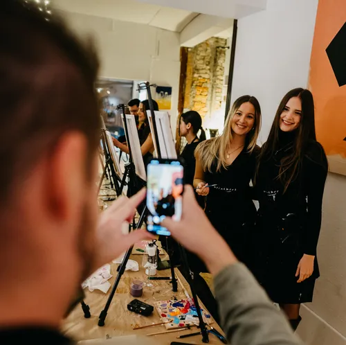 Two women posing, someone photographing with a phone.