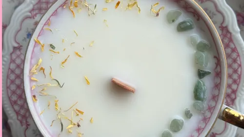 Kerze in Teetasse mit Blumen und Steinen.