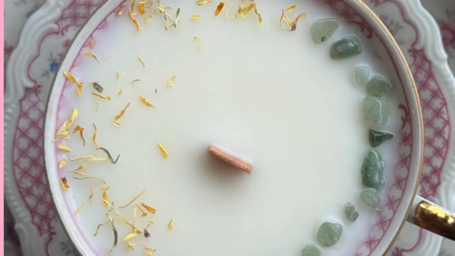 Kerze in Teetasse mit Blumen und Steinen.