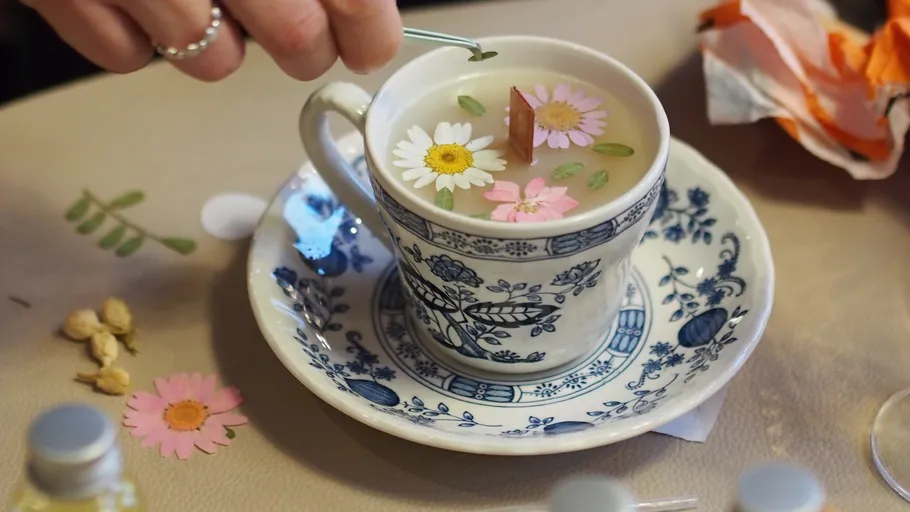 Floral tea in patterned cup, hand adding flowers.