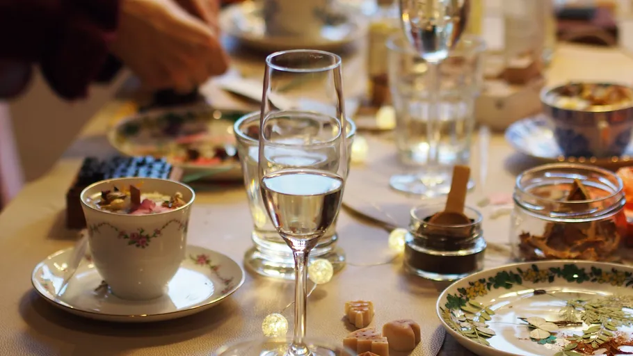 Table with glasses, dishes, and hands preparing food.