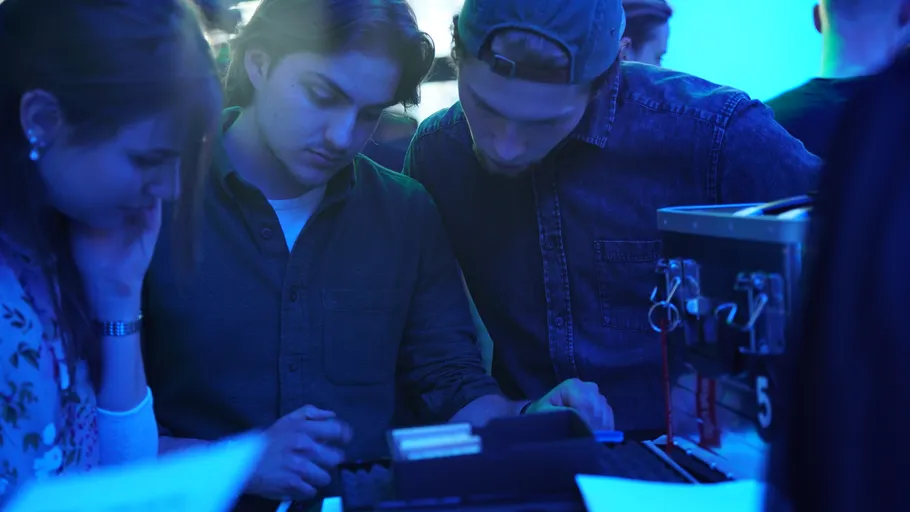 Three people concentrating on equipment in blue-lit room.
