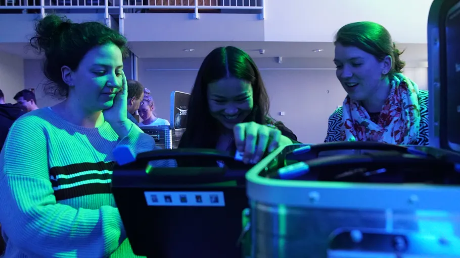 Three people examining tech equipment indoors.