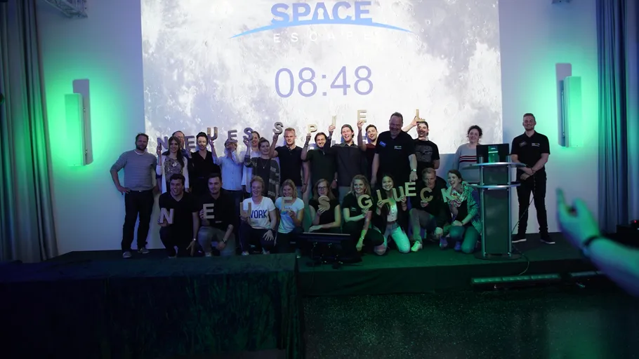 Gruppe posiert auf Bühne mit Weltraum-Hintergrund.