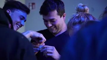 People smiling, assembling small object, blue lighting.