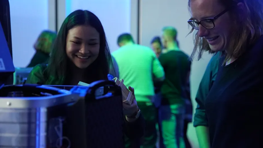 Two women smiling at machine, blue-lit room.