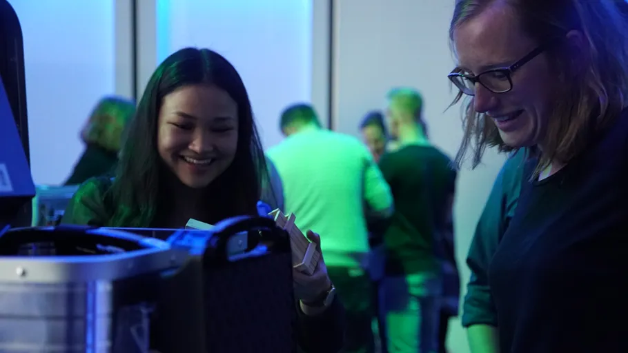 Two women smiling at device, indoor event.