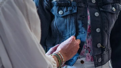 Hands adjusting buttons on denim jacket.