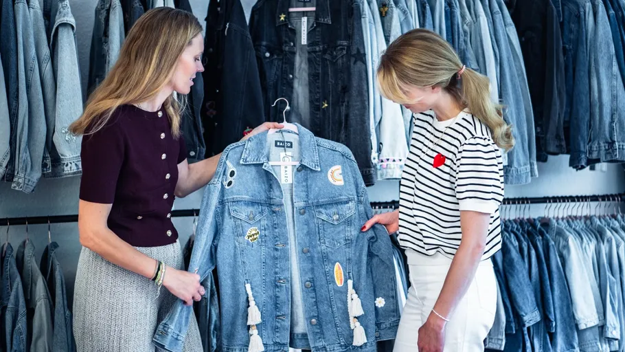 Two women examining a denim jacket in a store.