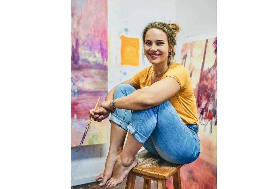 Woman smiling, sitting on stool in art studio.