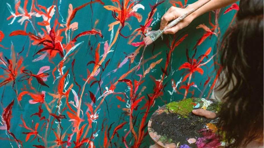 Person painting floral artwork on wall.