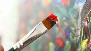 Pinsel mit roter Farbe nahe bunter Leinwand.