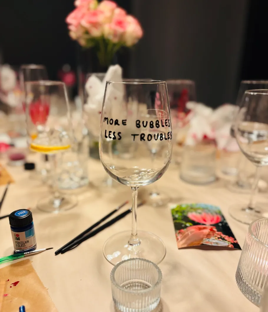 Dekoriertes Weinglas auf unordentlichem Basteltisch.