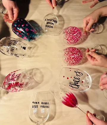 Hands hold decorated wine glasses on table.