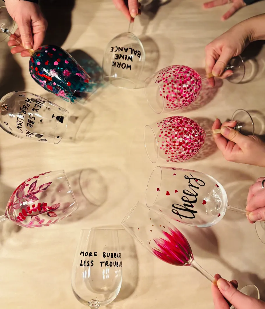 Hands hold decorated wine glasses on table.