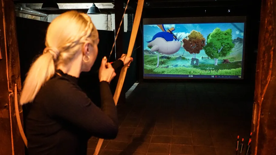 Person aiming bow at screen in indoor range.