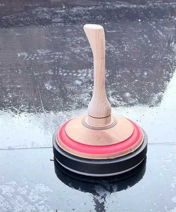 Wooden curling stone on icy surface.