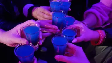 Hände stoßen mit blauen Getränkeschüssen an.