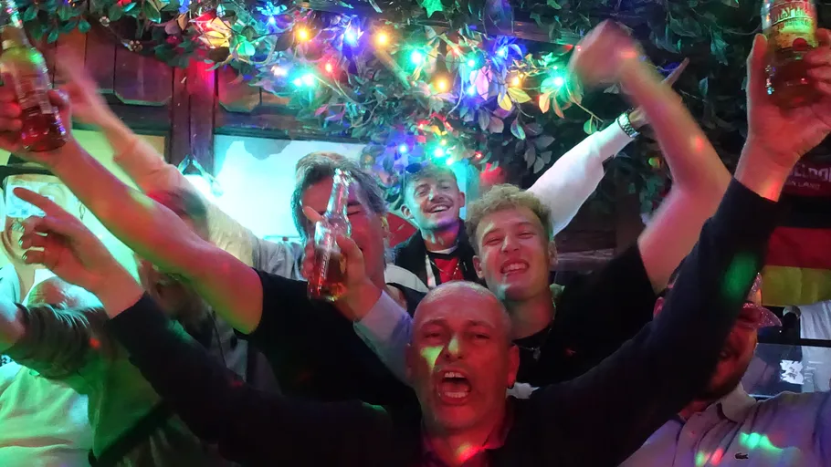 Gruppe feiert mit Getränken unter bunten Lichtern.