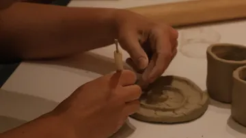 Hände formen Ton mit einem Werkzeug.