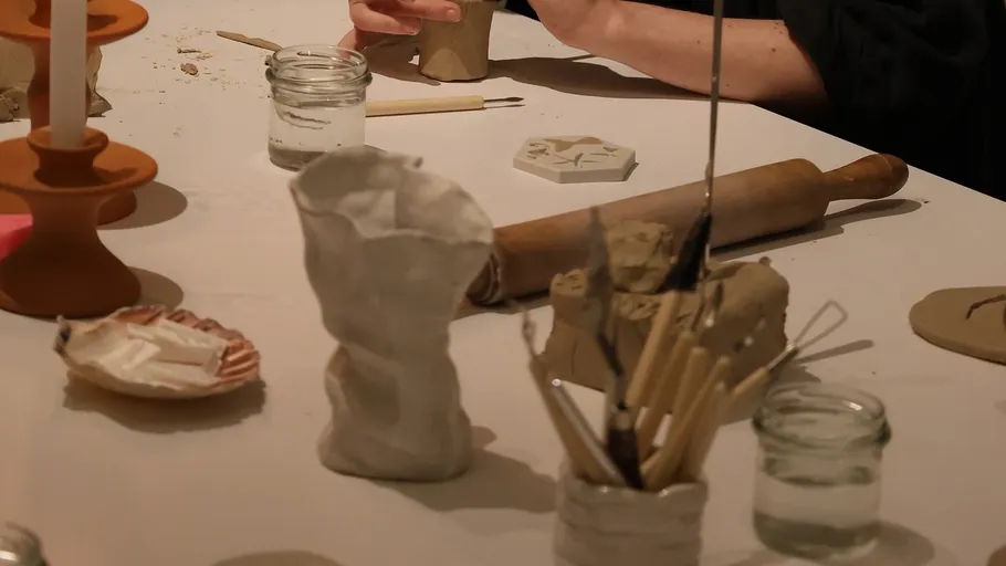 Hände modellieren Ton auf einem Basteltisch.
