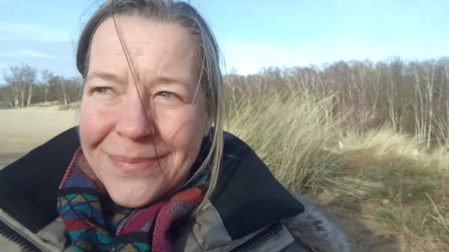 Frau lächelt draußen mit grasigem Hintergrund.