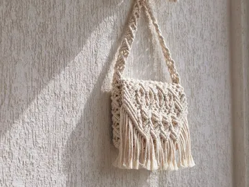Beige bag hangs on a bright wall in sunlight.
